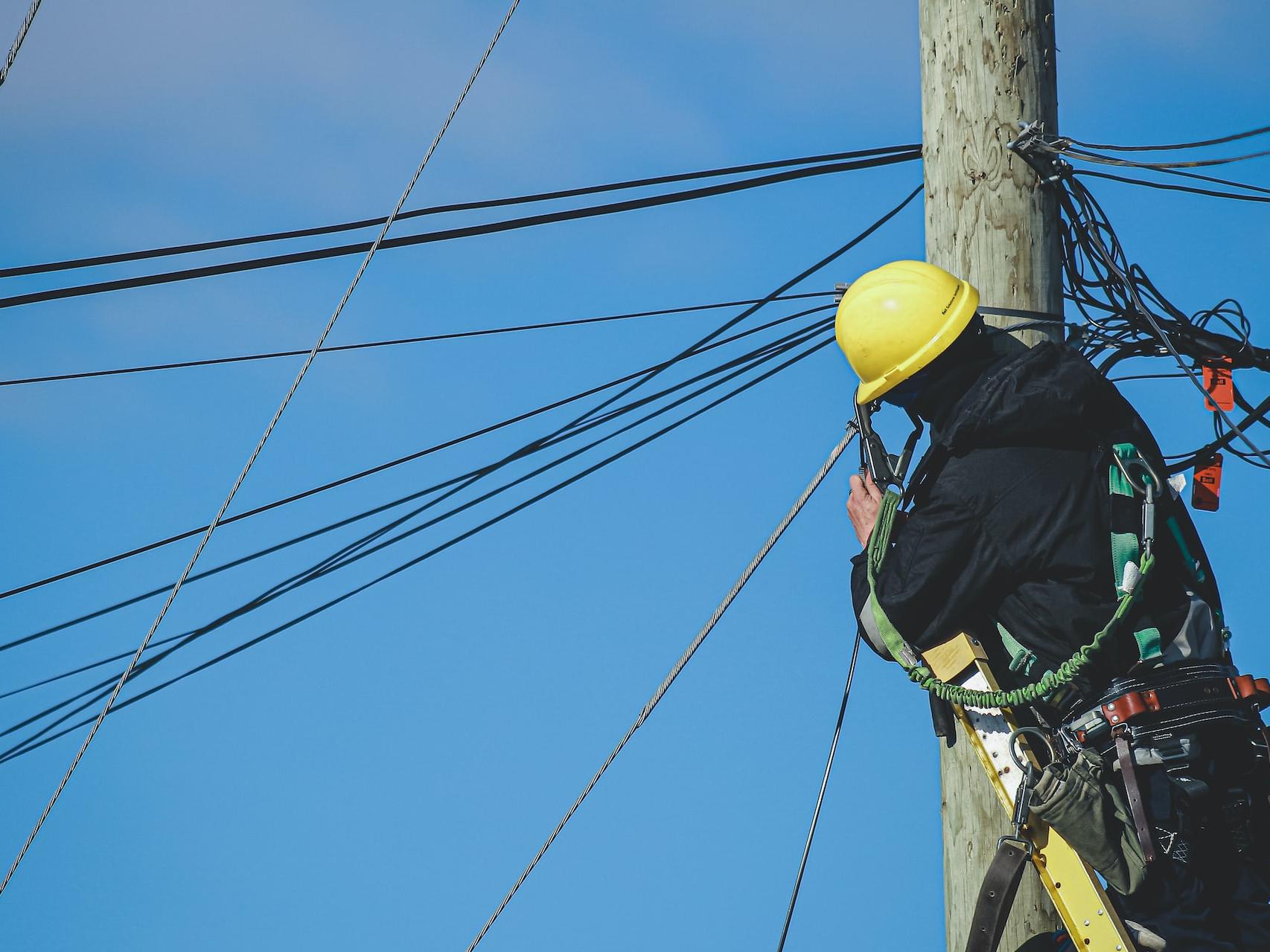 man in black jacket and yellow hard hat climbing on brown wooden post during daytime